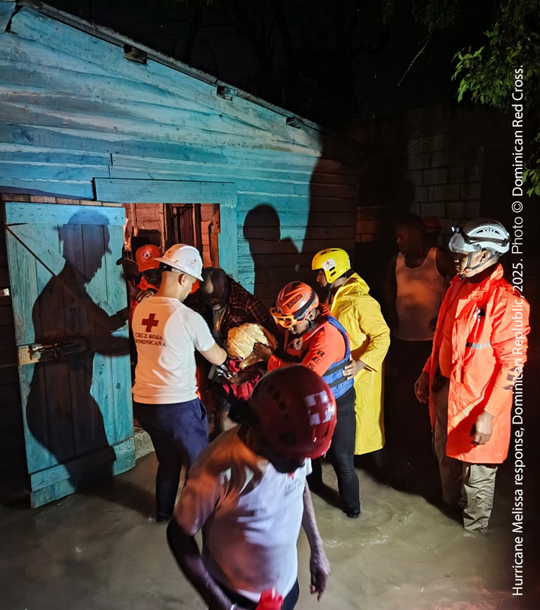 A group of Red Cross staff and emergency responders helping someone from their home at night.