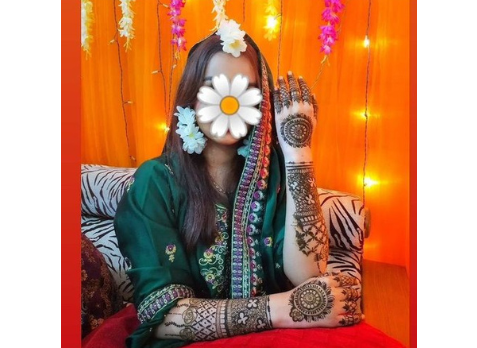 A young woman with complicated henna drawings on her arms sits in South Asian clothes. A flower covers her face in the picture to protect her identity.