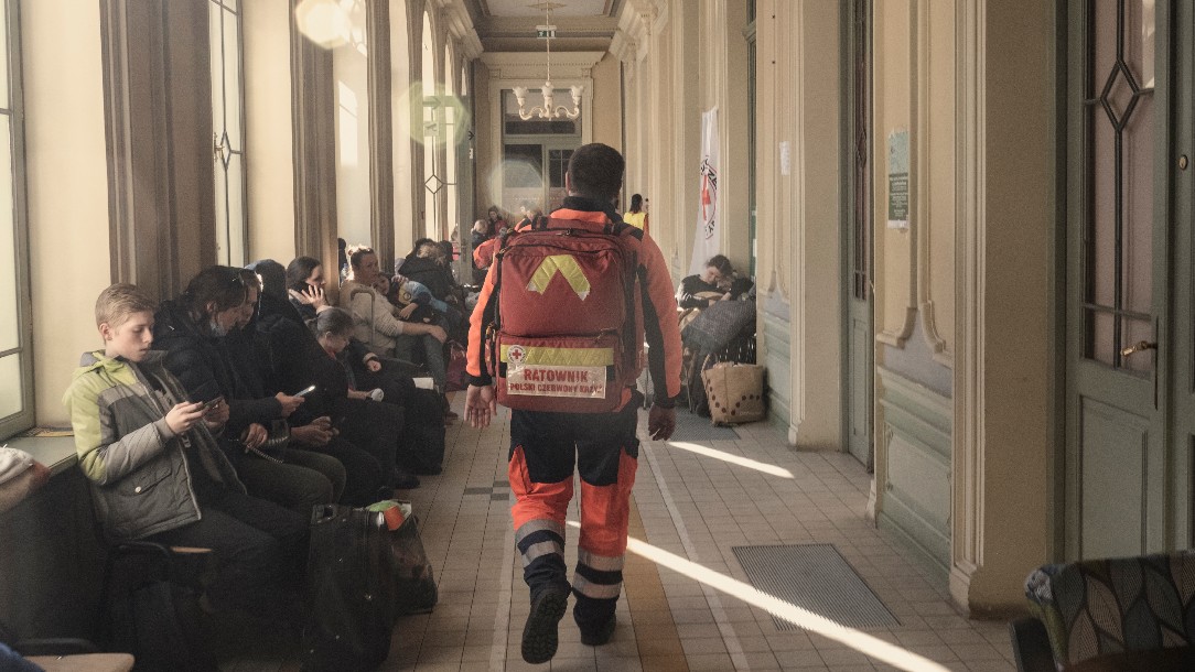 A Polish Red Cross volunteer, wearing a hi-vis suit and carrying a bag full of medical equipment, walks down a hallway at the Przemysl station in Poland, in March 2022