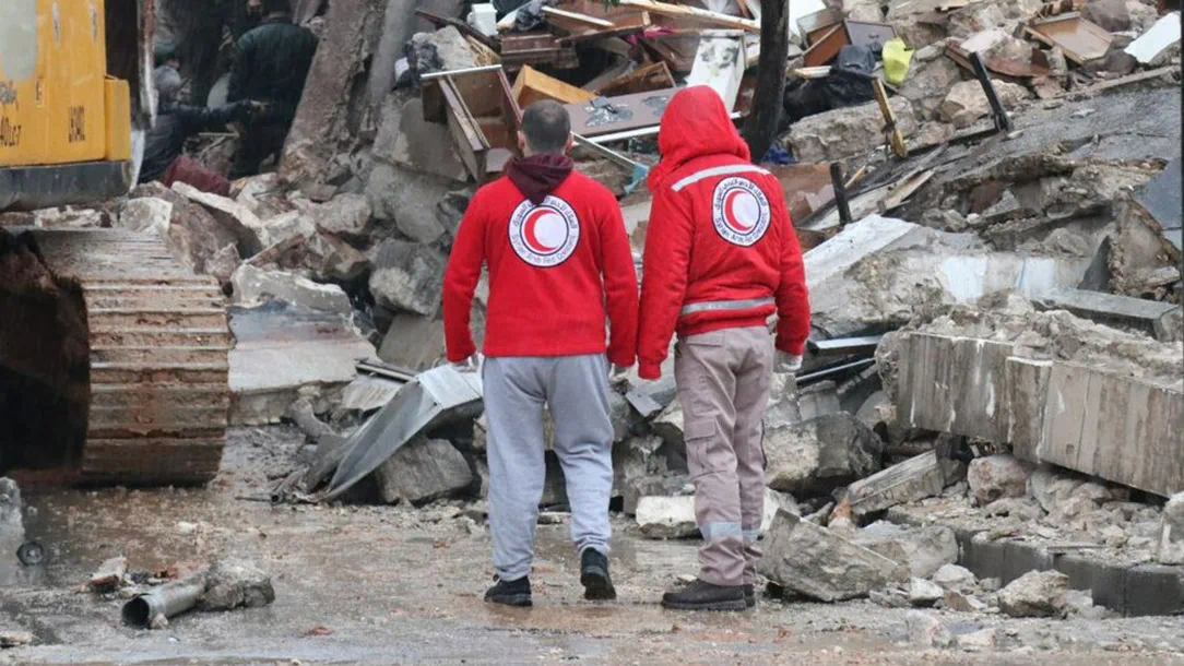 Two rescue workers from the Turkish Red Crescent stand facing rubble from the earthquake that hit Turkey and Syria.