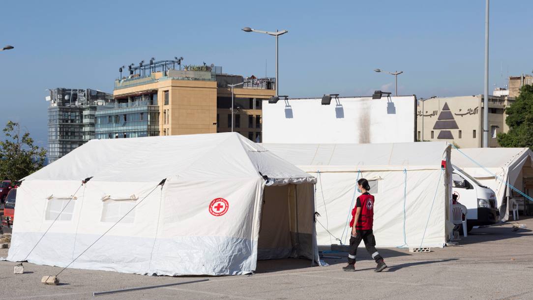 A Red Cross worker walks in a white medical tents with the Red Cross symbols.
