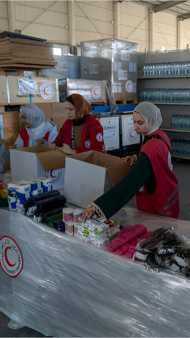 Women distribute aid with food and supplies in a warehouse.