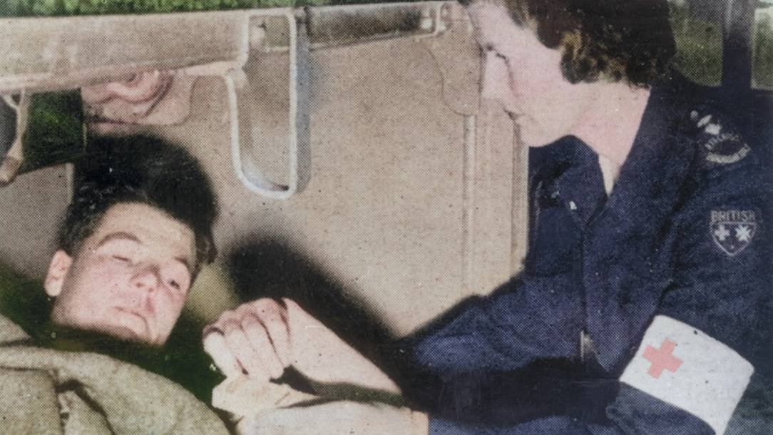 A British Red Cross welfare officer offers matches to a soldier, who is lying down