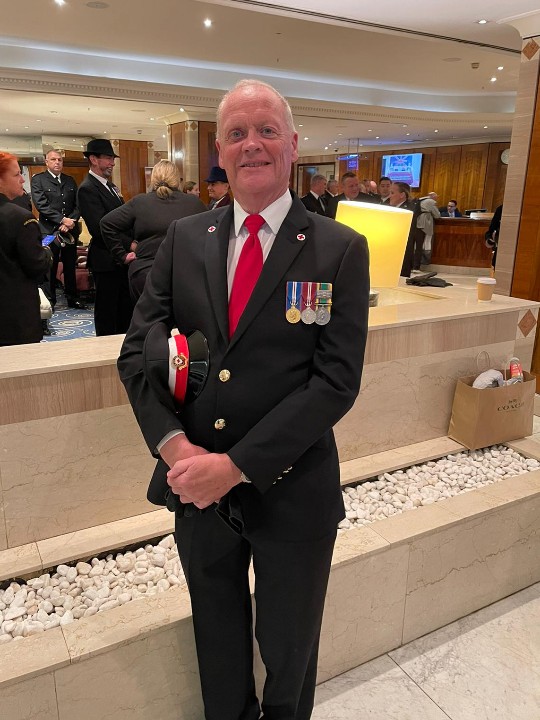 Ceremonial volunteer Andrew smiles at the camera wearing his British Red Cross ceremonial uniform, which is a grey suit with a white shirt and red tie