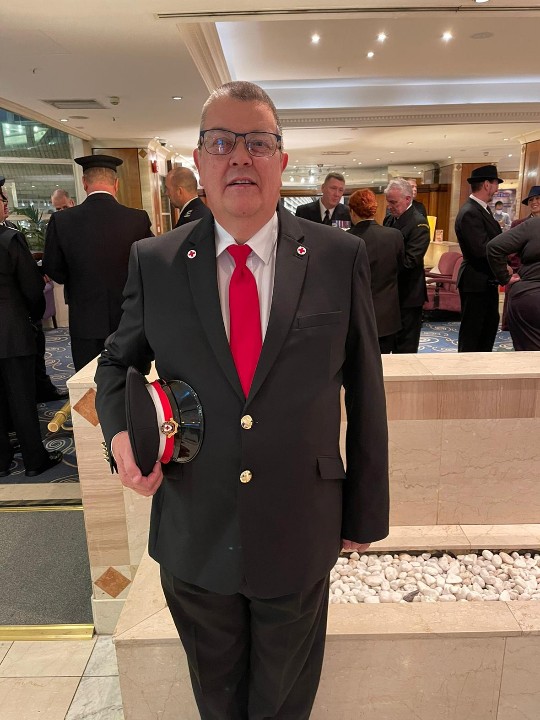 Volunteer Steve, wearing his ceremonial British Red Cross uniform of a grey suit with a red tie, faces the camera