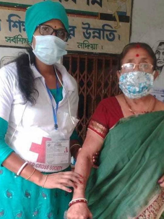 A Red Cross worker supports an older woman during the coronavirus pandemic.