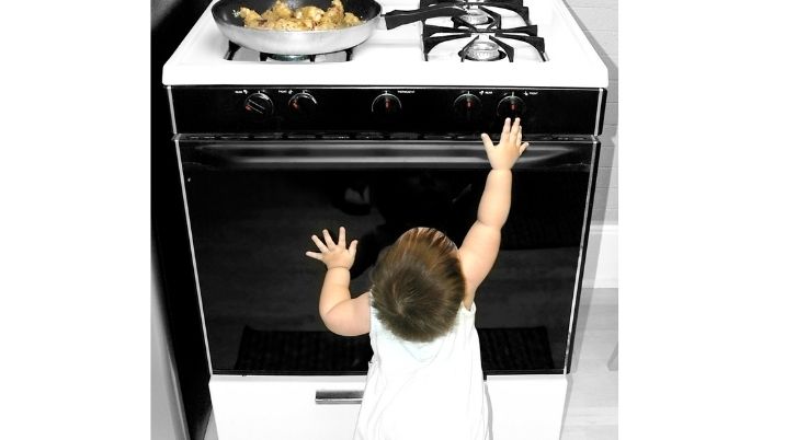 A baby reaching up towards a hot stove, in danger of burning herself.