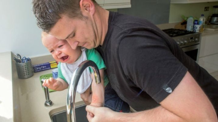 A man holds his baby's arm under the tap after it scalds itself.