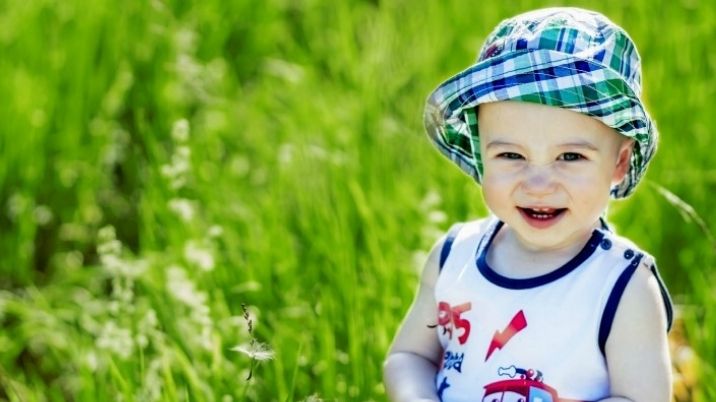 A baby happily sits in some long grass