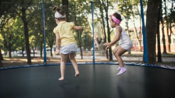Children bounce on a trampoline in the sunshine.