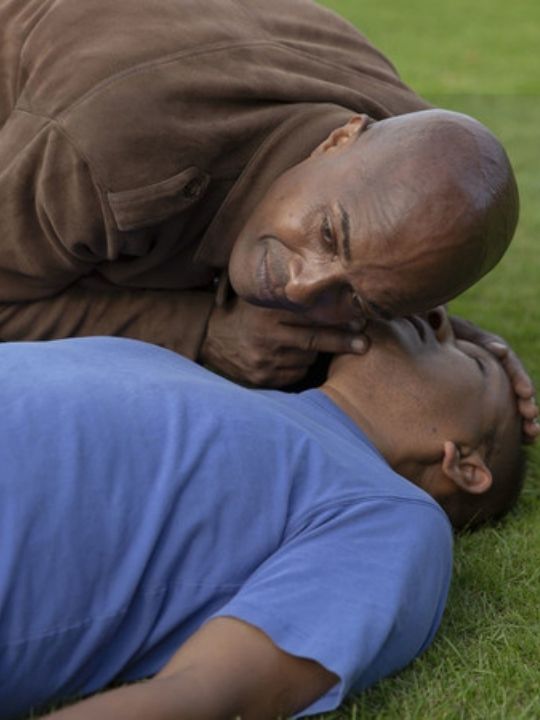An man checks to see whether an unresponsive man lying on the ground is breathing.