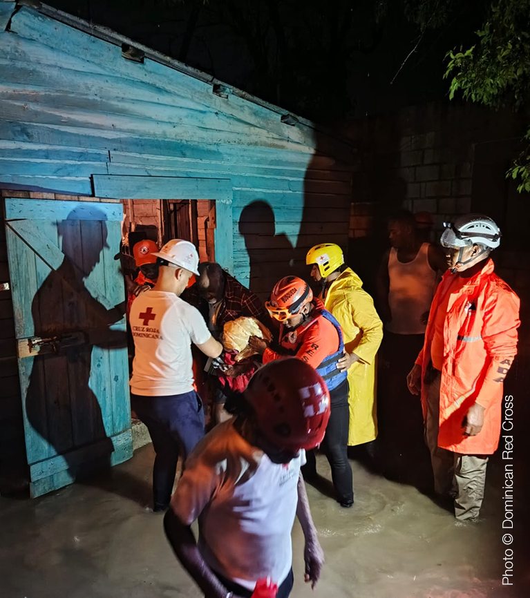 A photo of emergency responders and volunteers helping someone from their home at night.