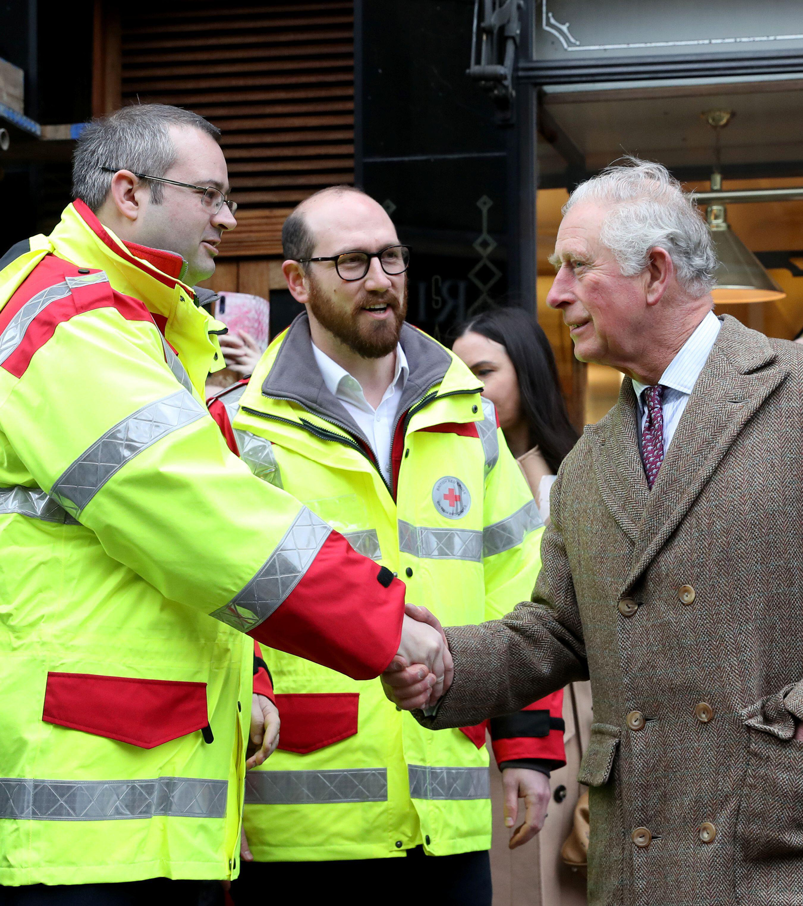 King Charles shakes hands with a British Red Cross volunteer while two others stand nearby.
