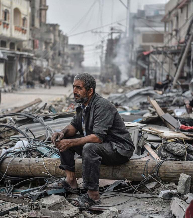 A man sits in rubble in Gaza, covered with dirt and soot.