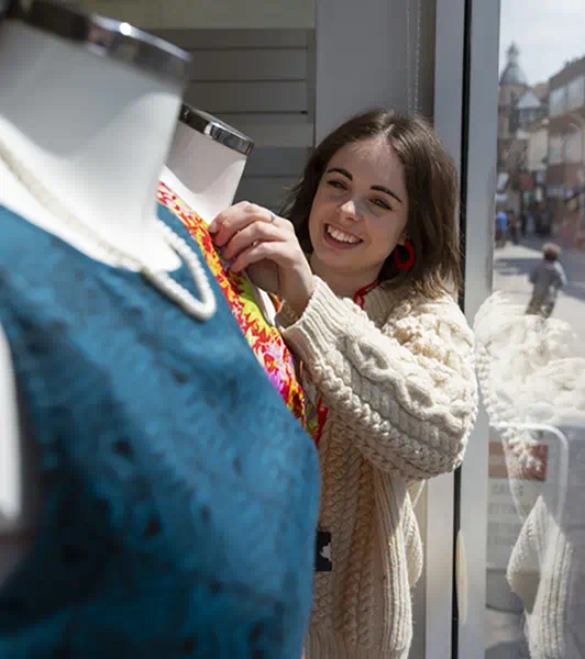 A volunteer adjusts a display in the window of a Red Cross charity shop.