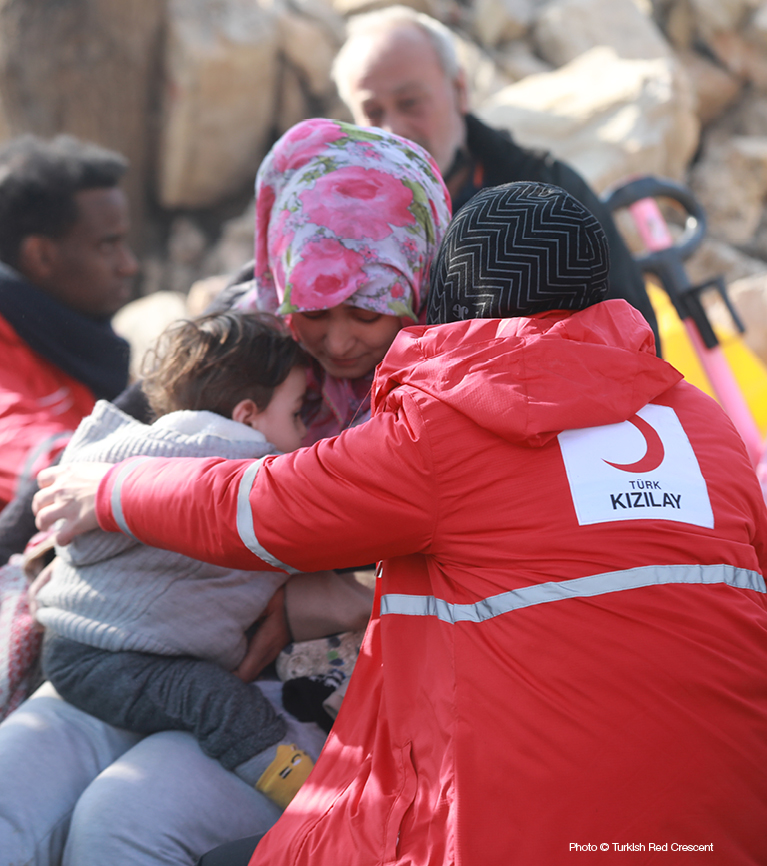 A Turkish Red Crescent volunteer hugs a family standing in front of rubble after the earthquakes.