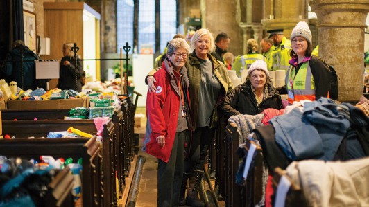 British Red Cross volunteers and people whose homes have been flooded stand together in a church surrounded by donated clothes and food.