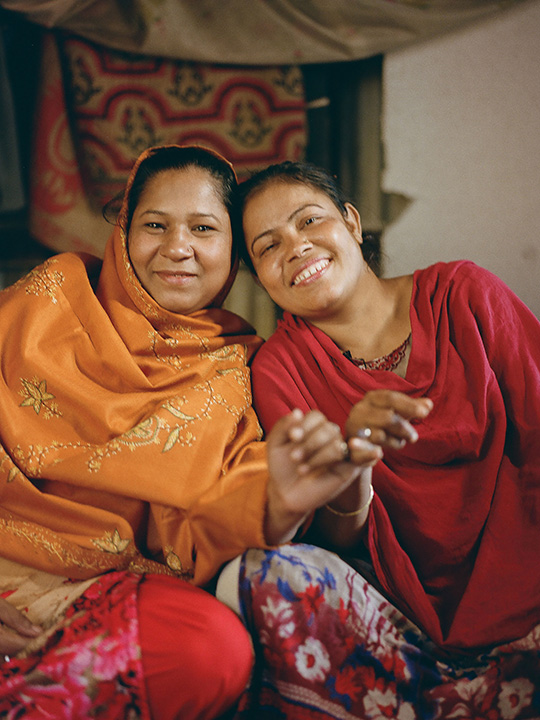 Josna and her friend Mahmouda in Barishal, Bangladesh, smile and lean against each other 