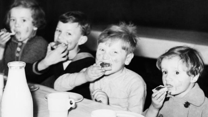 A black and white photograph showing young children tucking into jelly and cake at a table.