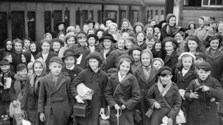 A black and white photograph showing a group of evacuated children at a train station.