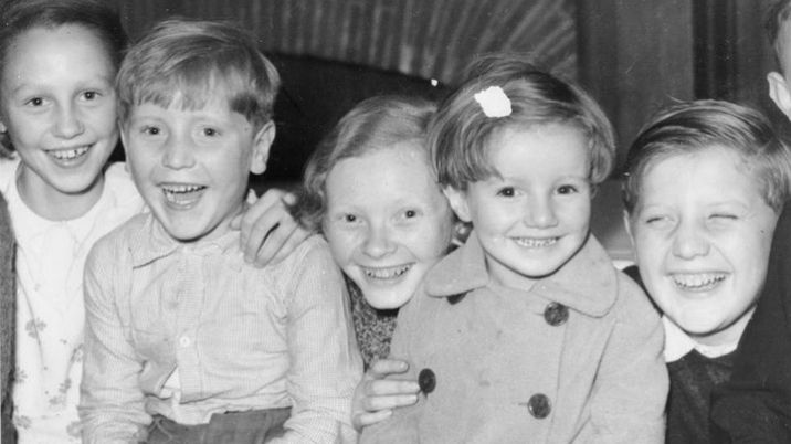 A black and white photograph showing a group of evacuated children smiling at the camera