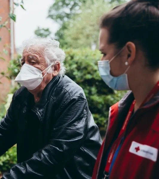A British Red Cross volunteer helps an elderly man back to his house.