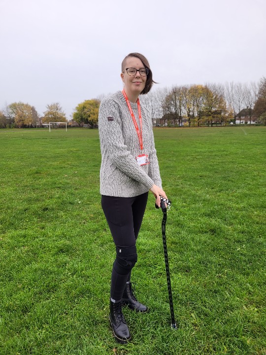 Krystal stands on an area of grass holding on to a walking stick