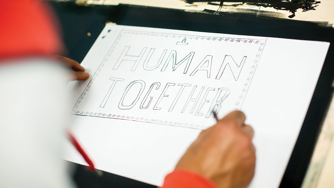 Someone draws the words 'human together' at an art workshop.