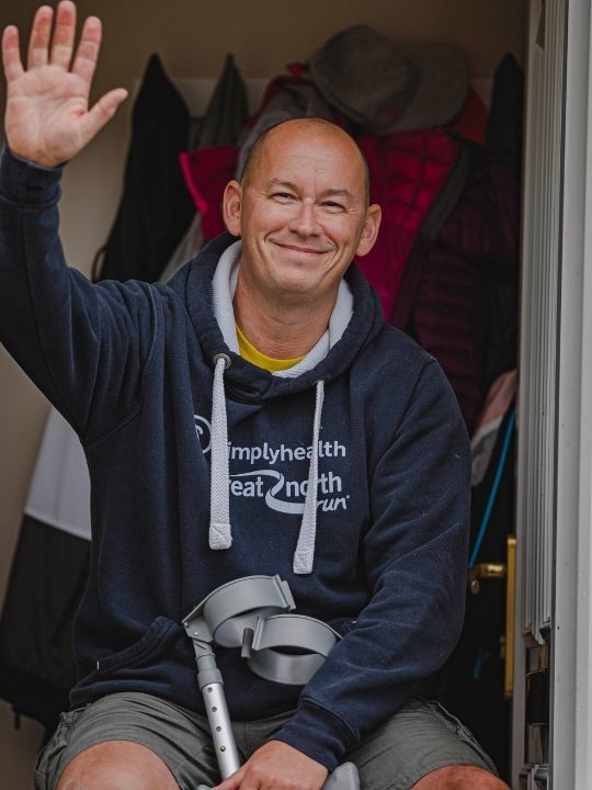 A wheelchair service user with crutches waves at the camera.