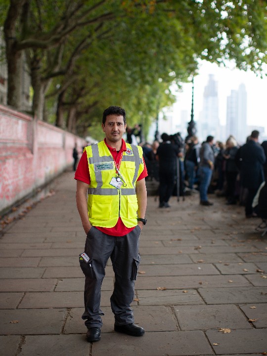 A British Red Cross volunteer in uniform smiles at the camera while standing a pavement overlooking the River Thames