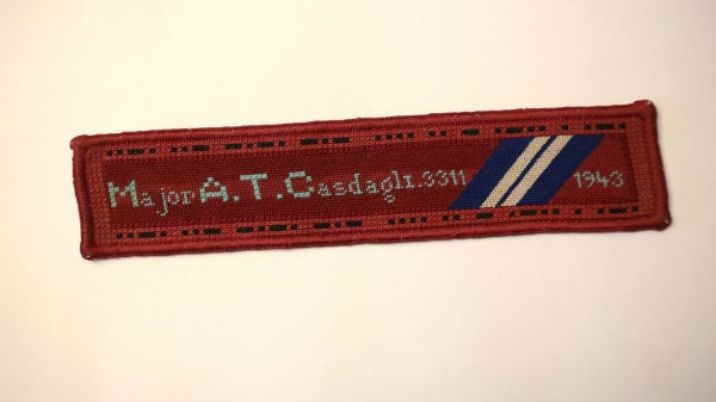 An embroidered bookmark in Harrow colours bearing the phrase 'fuck Hitler' in Morse code, by prisoner of war, Alexis Casadagli.