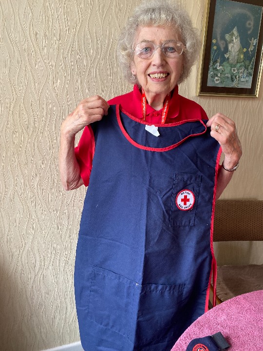 Volunteer Patricia faces the camera holding her old Red Cross uniform, a navy blue tabard