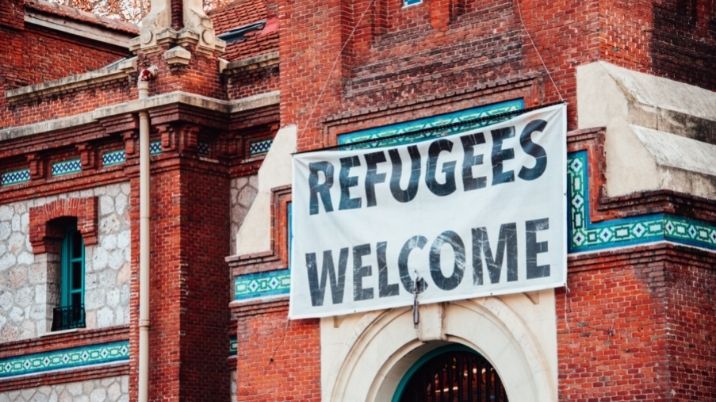 An old public building with a banner and the words 'Refugees welcome' on it.