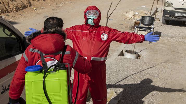 Member of the Syrian Arab Red Crescent disinfecting another member's uniform