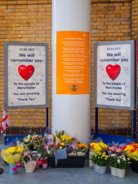 A memorial for the victims of the Manchester bombing, with flowers and a poster featuring the Manchester bee symbol.