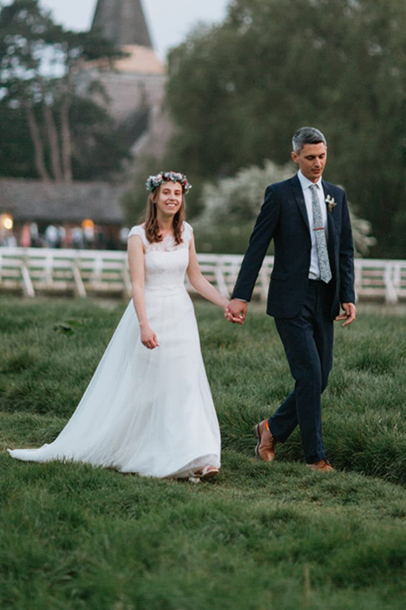 Laura Trower wearing the wedding dress she bought at a British Red Cross charity shop, walking in a green field with her new husband.