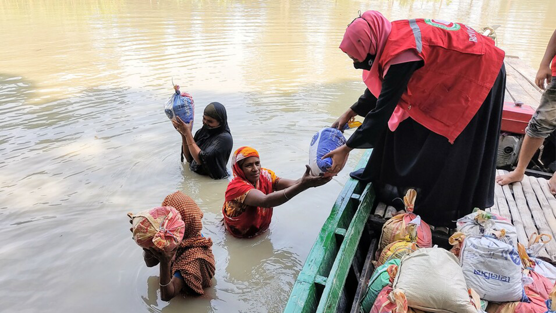 Women including a Red Cross volunteer pass sandbags to each other, surrounded by floodwater