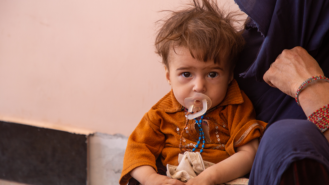 A children in Afghanistan sits against his mother's knee. © IFRC.