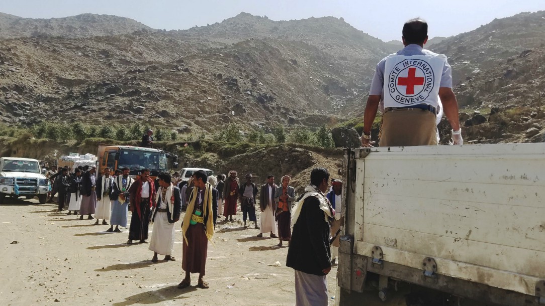 People stand two metres apart in a queue while a Red Cross worker hands out packages from the back of a truck. 