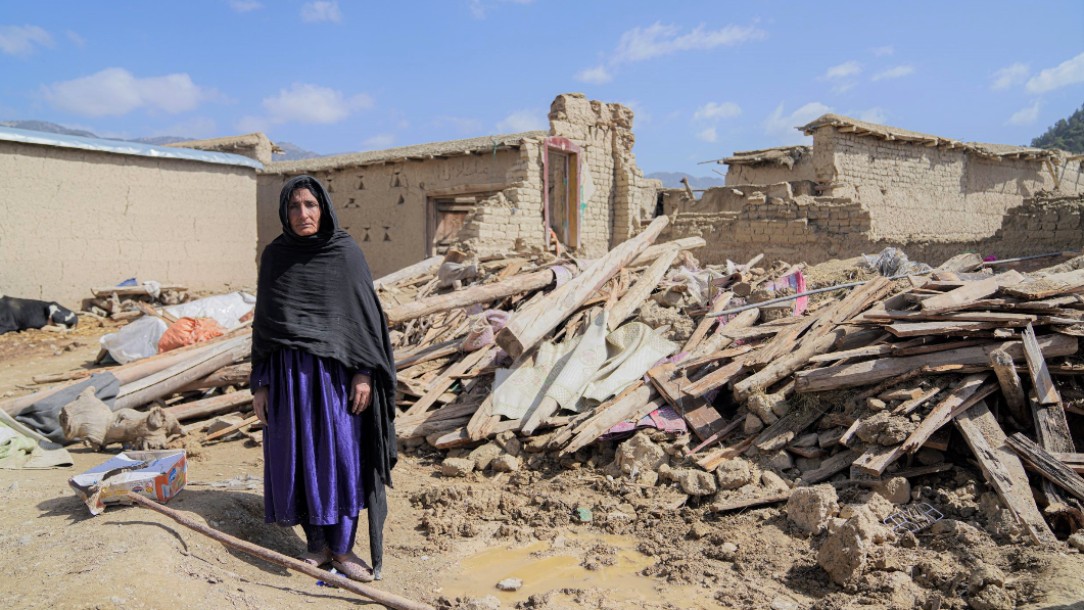 A woman stands facing the camera while stood in front of rubble following an earthquake in Afghanistan