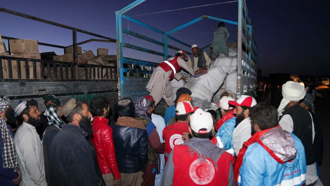 People wait for relief items to be taken off of truck following Afghanistan earthquake.