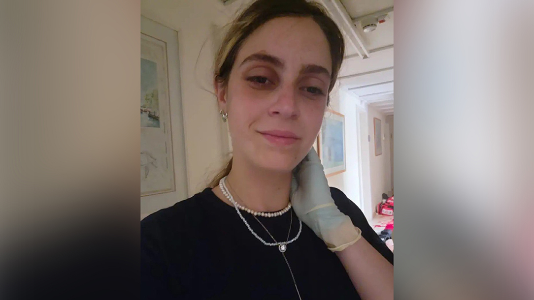 Amit is taking a selfie. She has her hair tied back and is wearing necklaces, a black t-shirt and white medical gloves