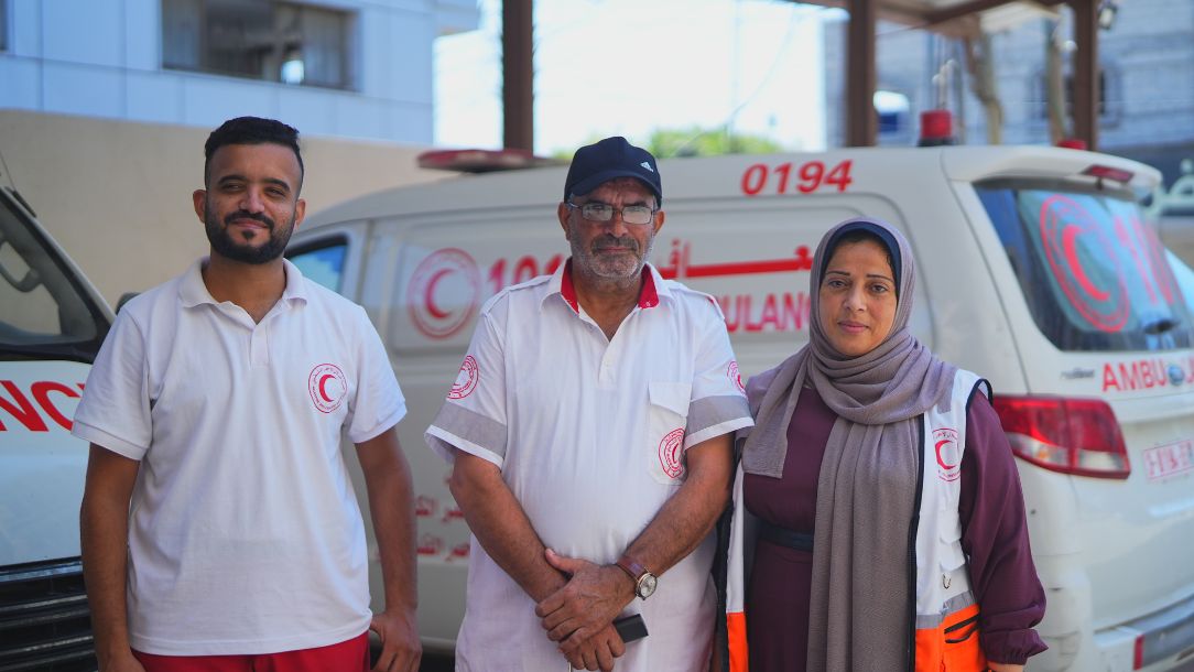 Awni and his family - all Palestine Red Crescent Society responders - stand in front of an ambulance, dressed in their uniforms.