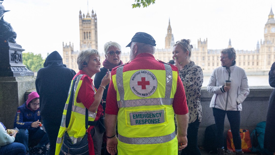Lyn and Barrie, both wearing their Red Cross uniforms, talk to members of the public waiting in the queue to see Her Majesty the Queen
