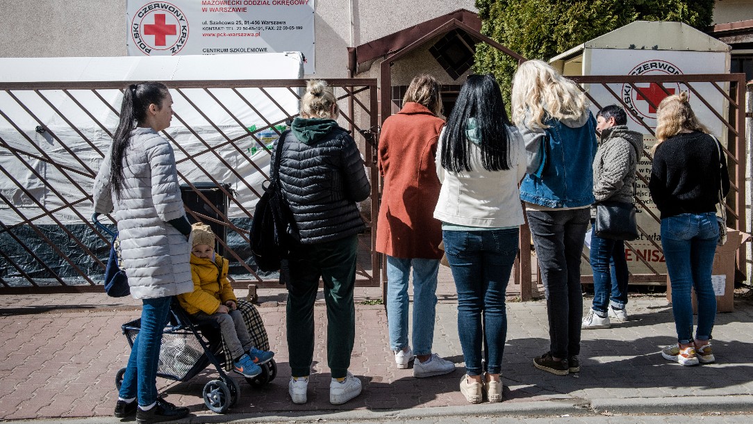A queue of people stand outside a building in Poland, waiting to receive cash assistance from the Polish Red Cross
