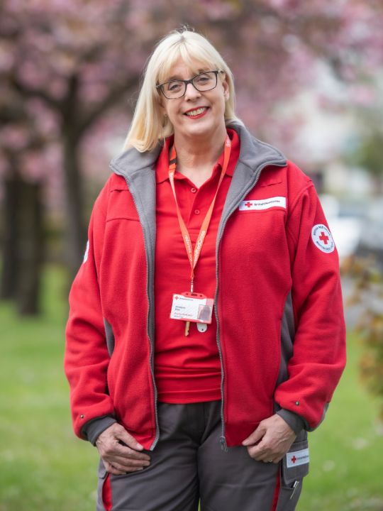 Volunteer Christine stands underneath blossom trees in her British Red Cross uniform.