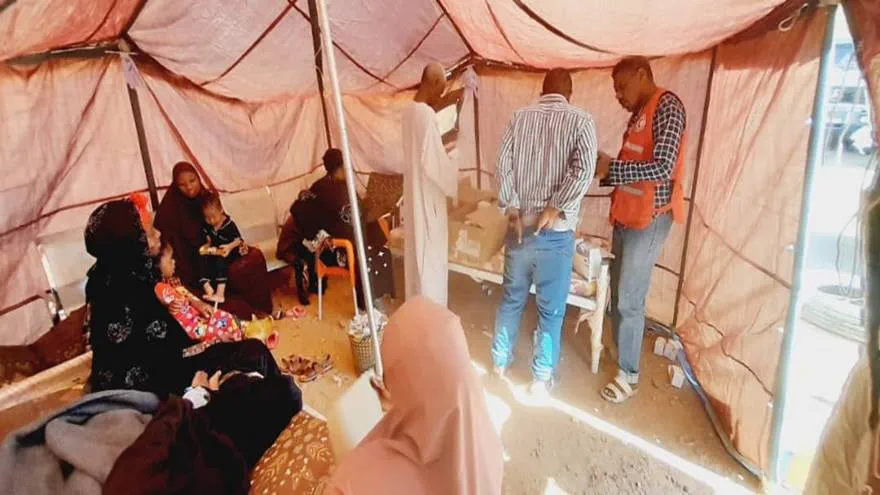 Volunteers and Sudanese people gather in a thin material tent
