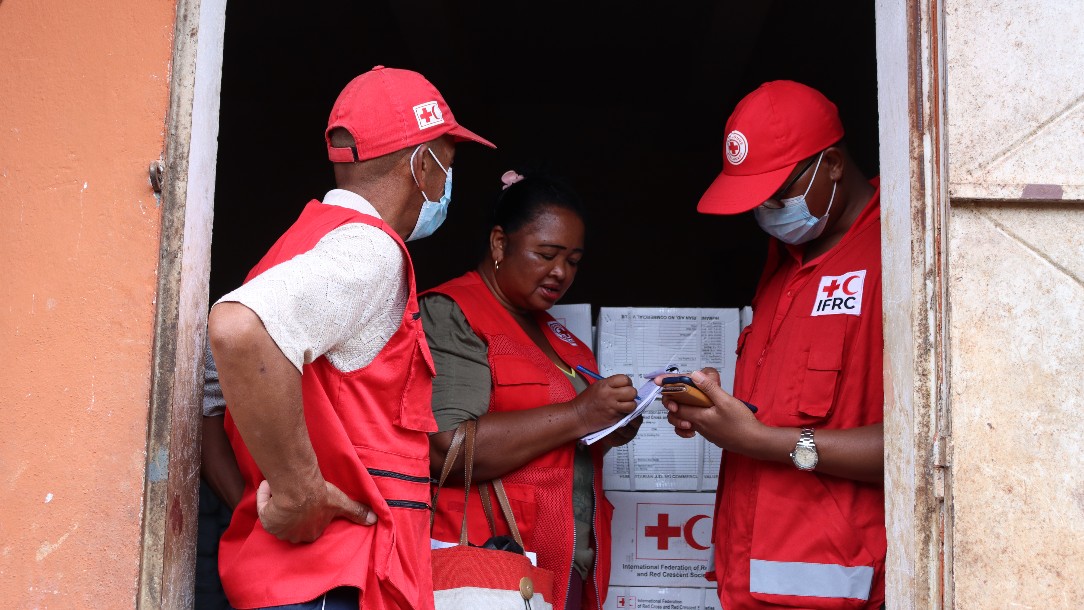 Three members of the Malagasy Red Cross/IFRC wearing their uniform stand at the doorway of a building 