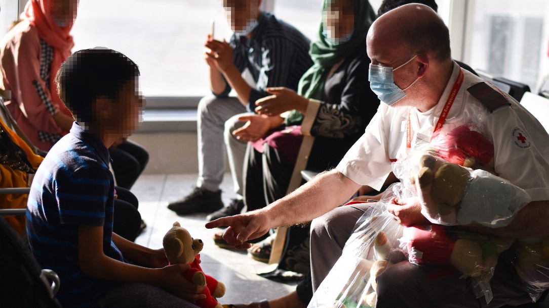 A man in a British Red Cross uniform hands out stuffed animals to the children of families who have recently arrived from Afghanistan