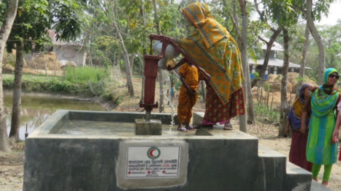 A woman uses a water pump bearing a Red Cross and Red Crescent emblem in Bangladesh.